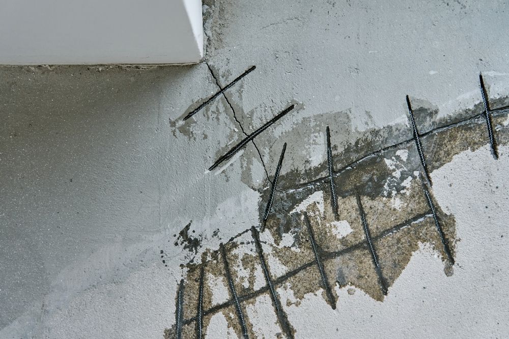 Cracked concrete surface with exposed rebar and crumbling gray plaster near a wall