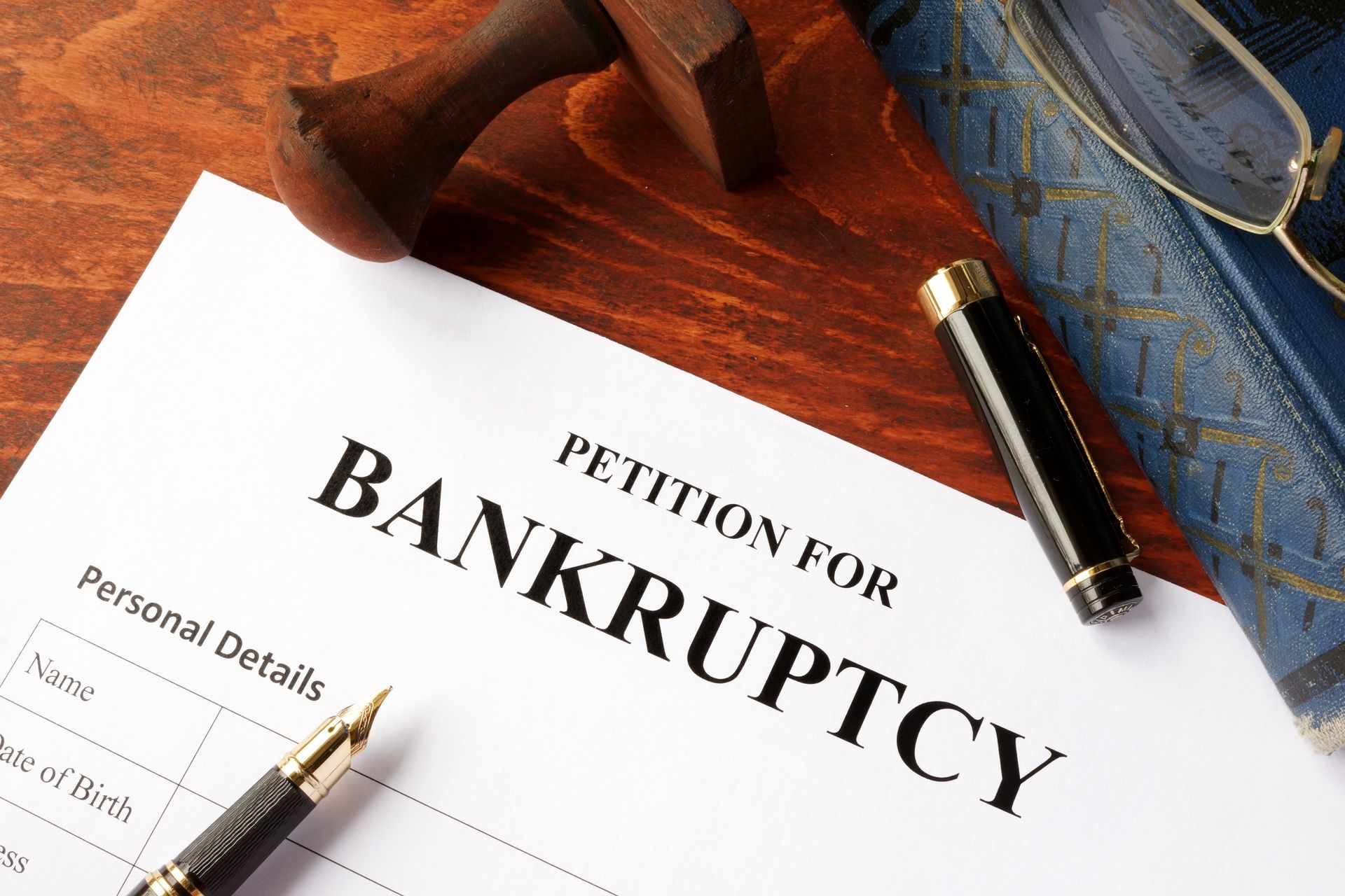 Bankruptcy petition form with pen, stamp, and eyeglasses on wooden desk.