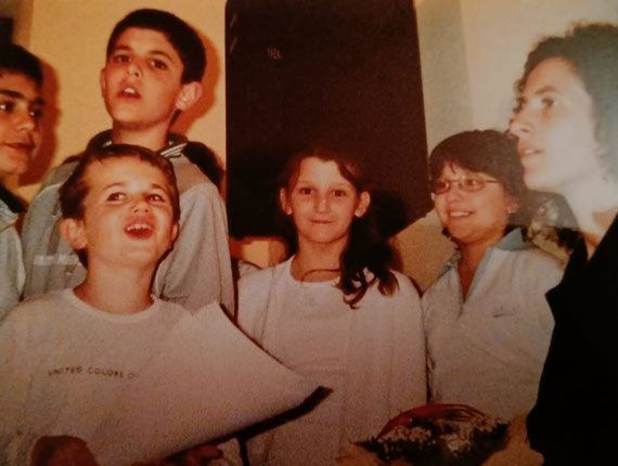 Un gruppo di persone al chiuso, sorridenti e intente a cantare insieme in una stanza illuminata da una luce calda.