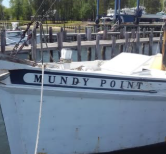 A white boat named MUNDY POINT docked at a wooden pier on a bright day. A white boat named MUNDY POINT docked at a wooden pier on a bright day.