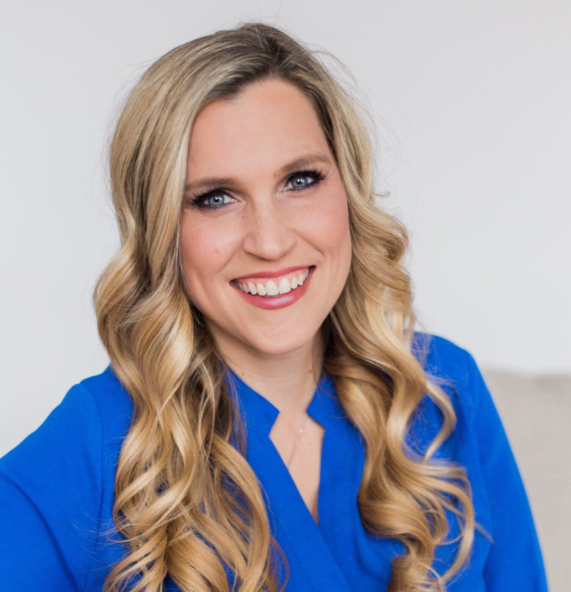A woman with blonde hair is wearing a blue shirt and smiling.