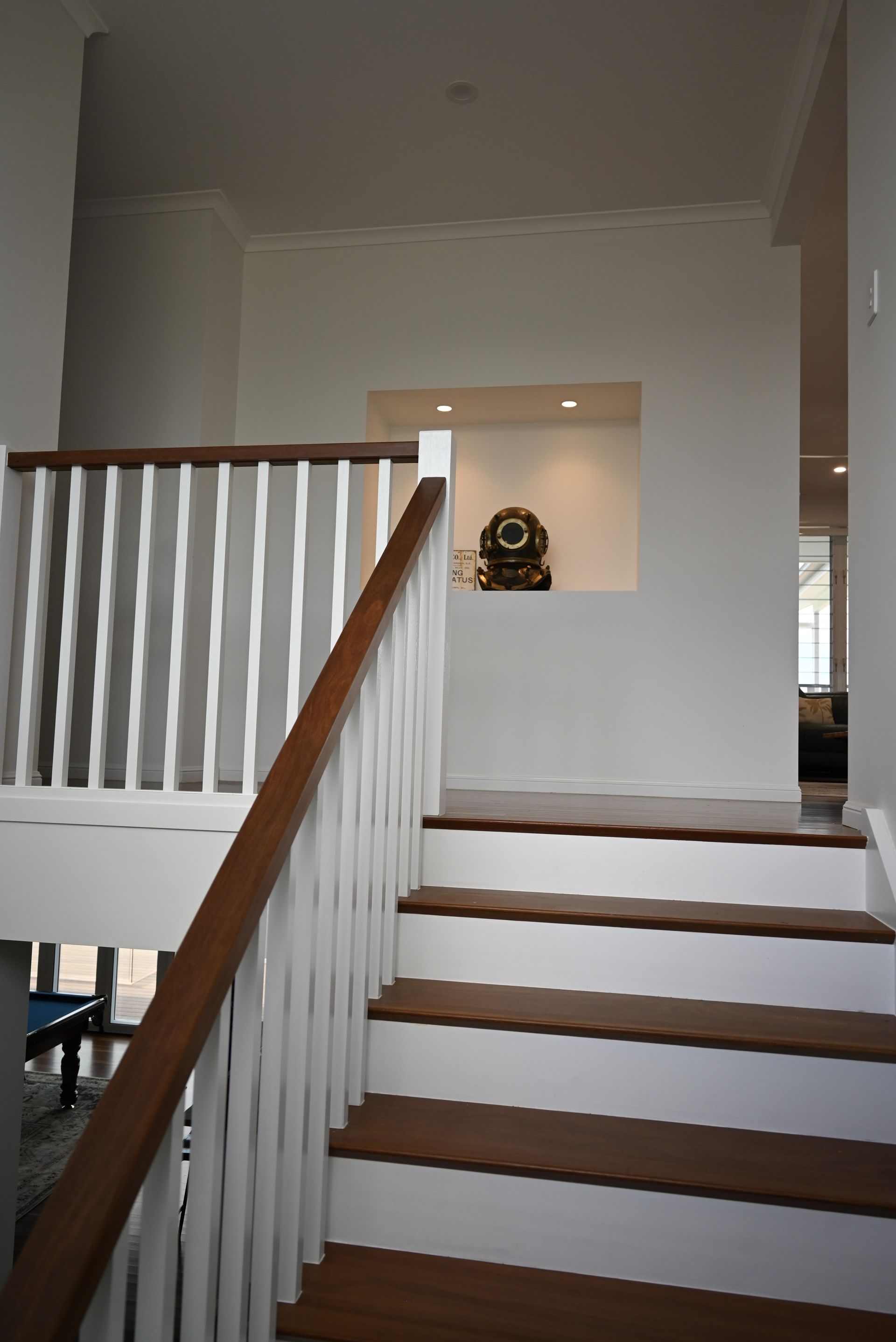 Indoor staircase with white railings, wooden steps, and a small wall niche holding a decorative clock.