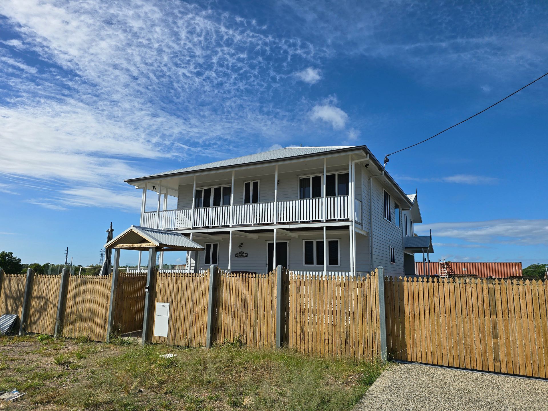 Two-story white house behind a wooden fence under a bright blue sky
