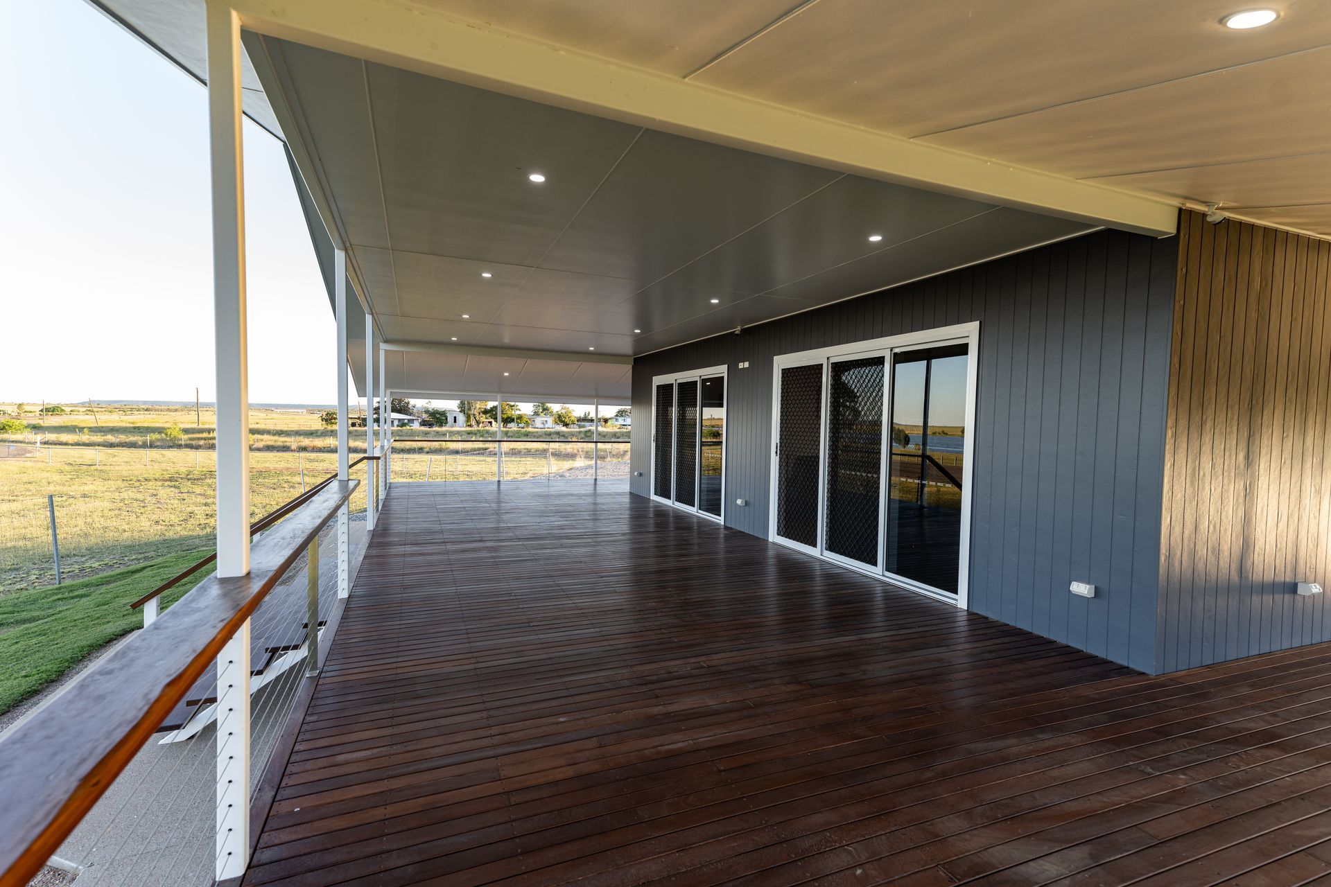 Covered wooden deck beside a modern building with glass doors and a view of open fields
