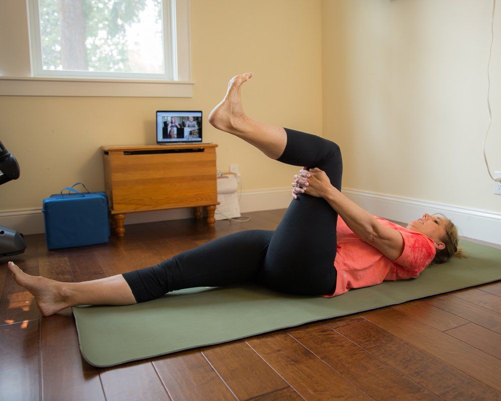 A woman is laying on a yoga mat with her legs crossed.