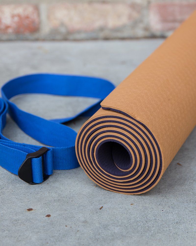 A yoga mat is rolled up next to a blue strap