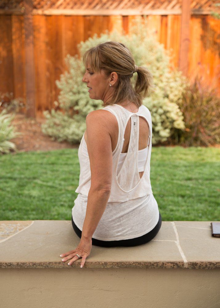 A woman in a white tank top is sitting on a bench.