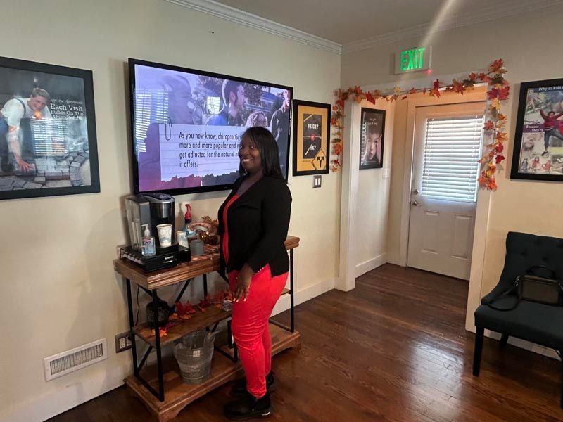 Woman standing beside a TV in a decorated living room, holding a phone and facing the screen.