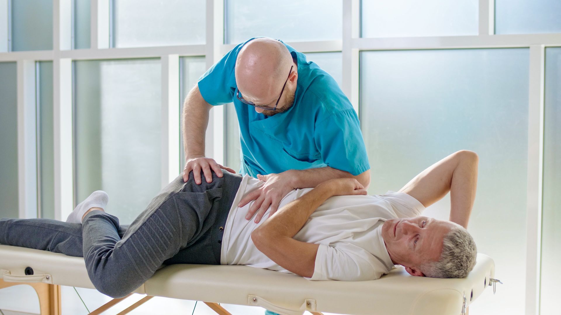 Physical therapist helping a man stretch on a treatment table in a bright clinic room