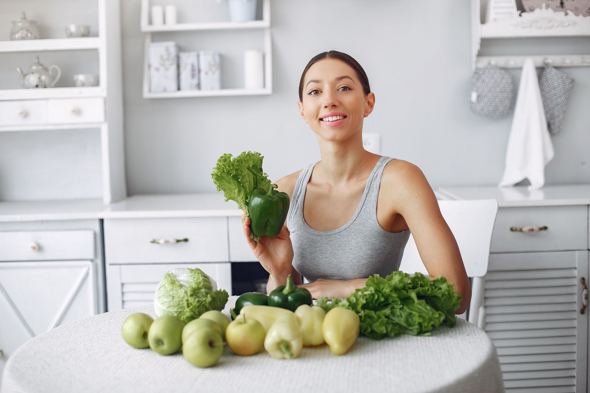Woman in a bright kitchen holding kale beside apples and leafy greens on a table