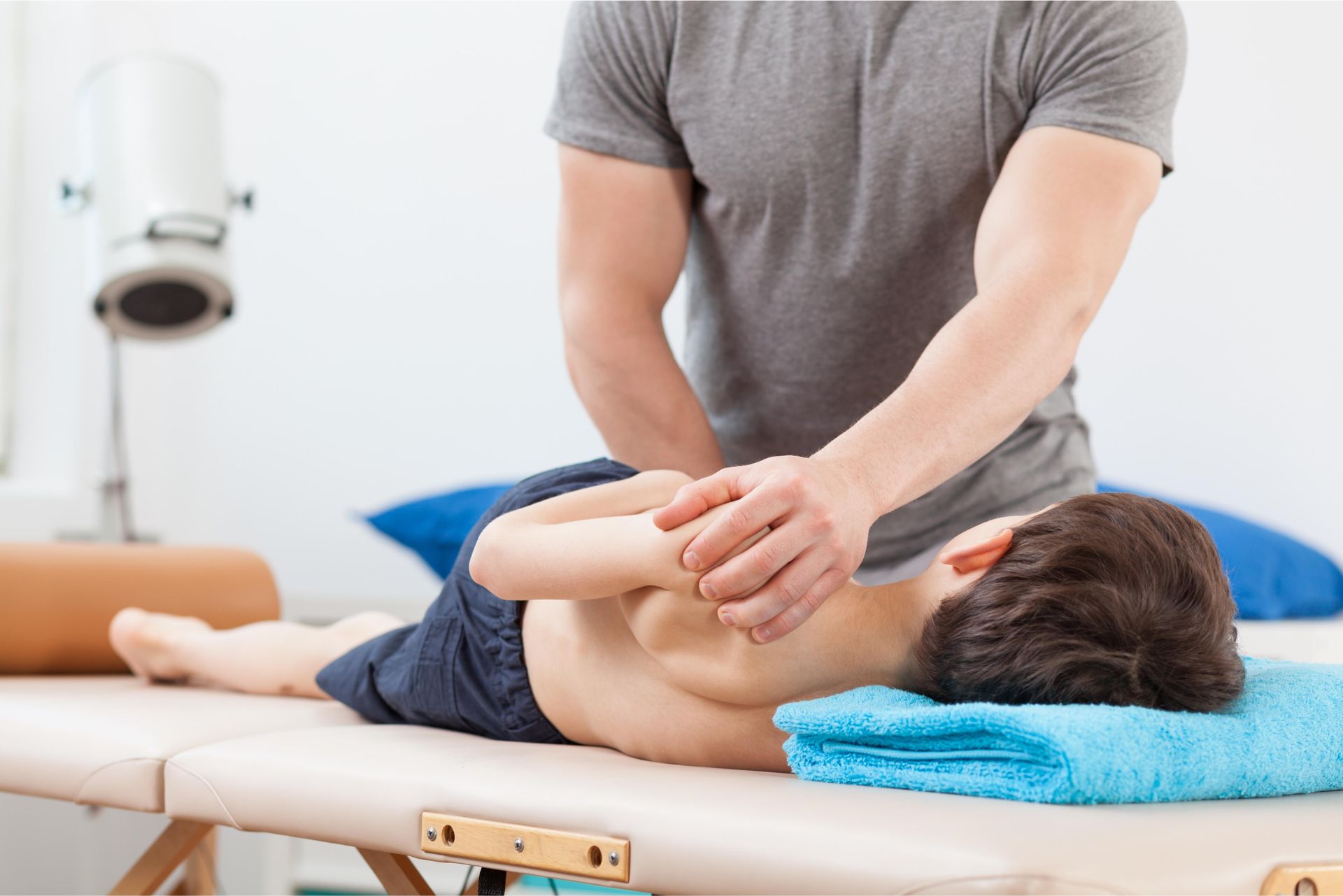 Child receiving a back massage from a therapist on a treatment table, in a bright clinic room