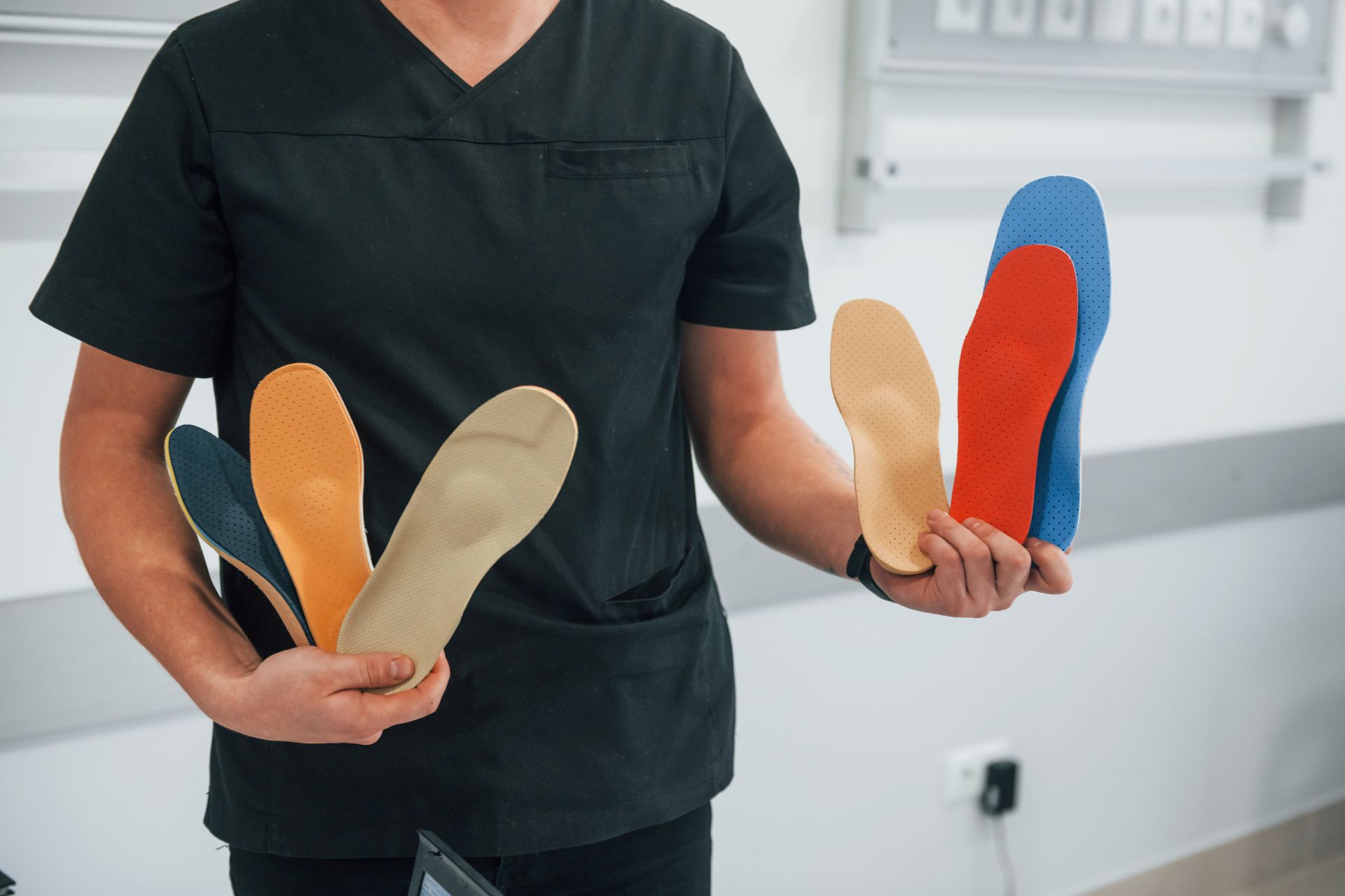 Person in black scrubs holding several colorful orthotic insoles in a bright clinic setting
