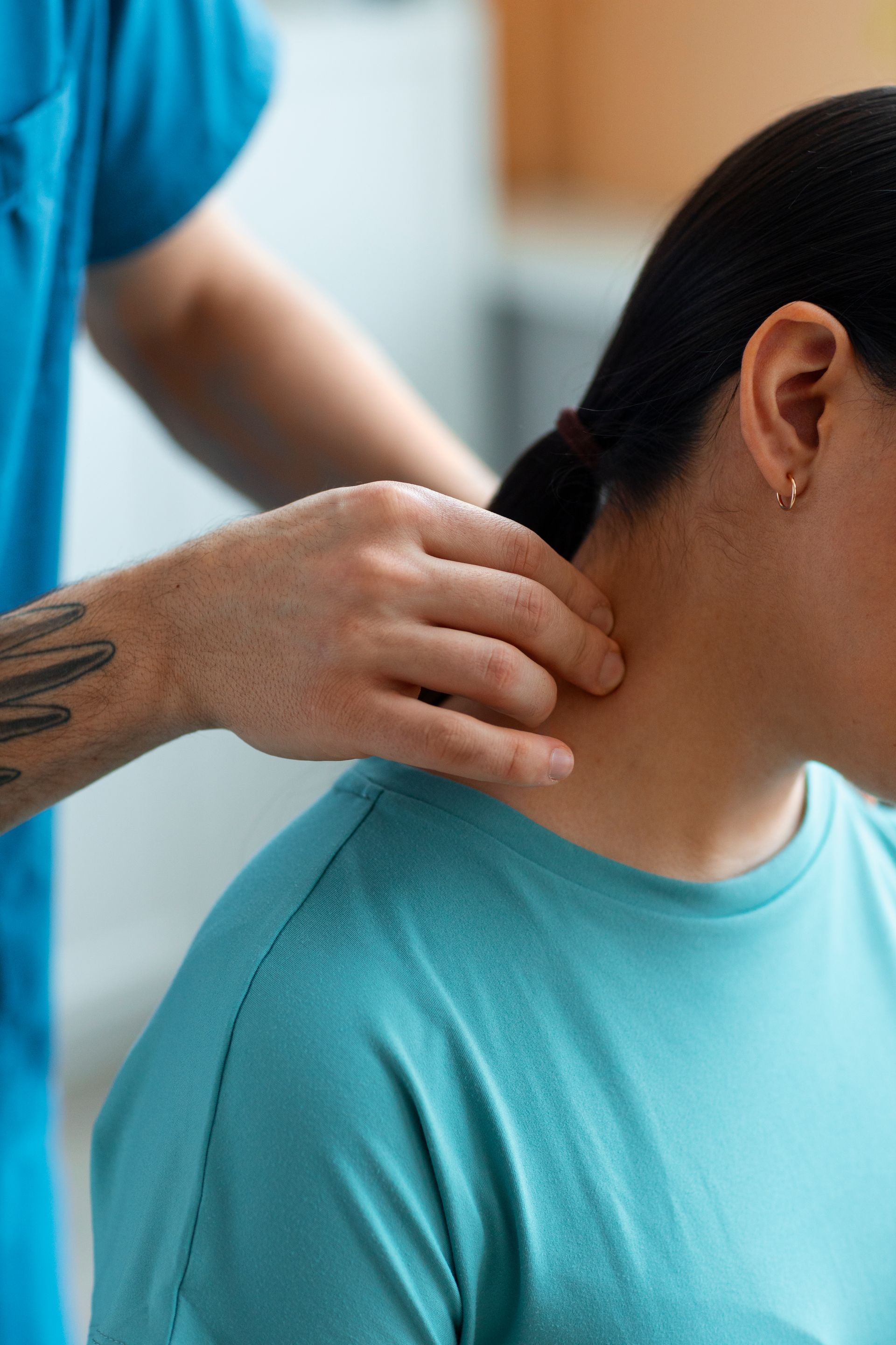 Hands massaging the neck of a person in a turquoise shirt, likely during a therapy session.