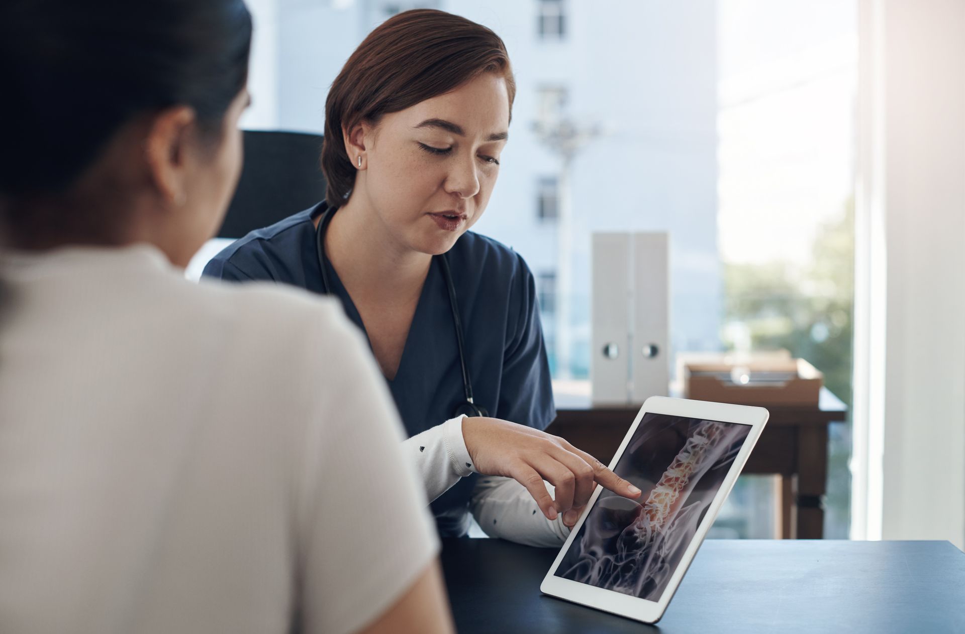 Woman pointing at a tablet screen during a discussion in a bright office.