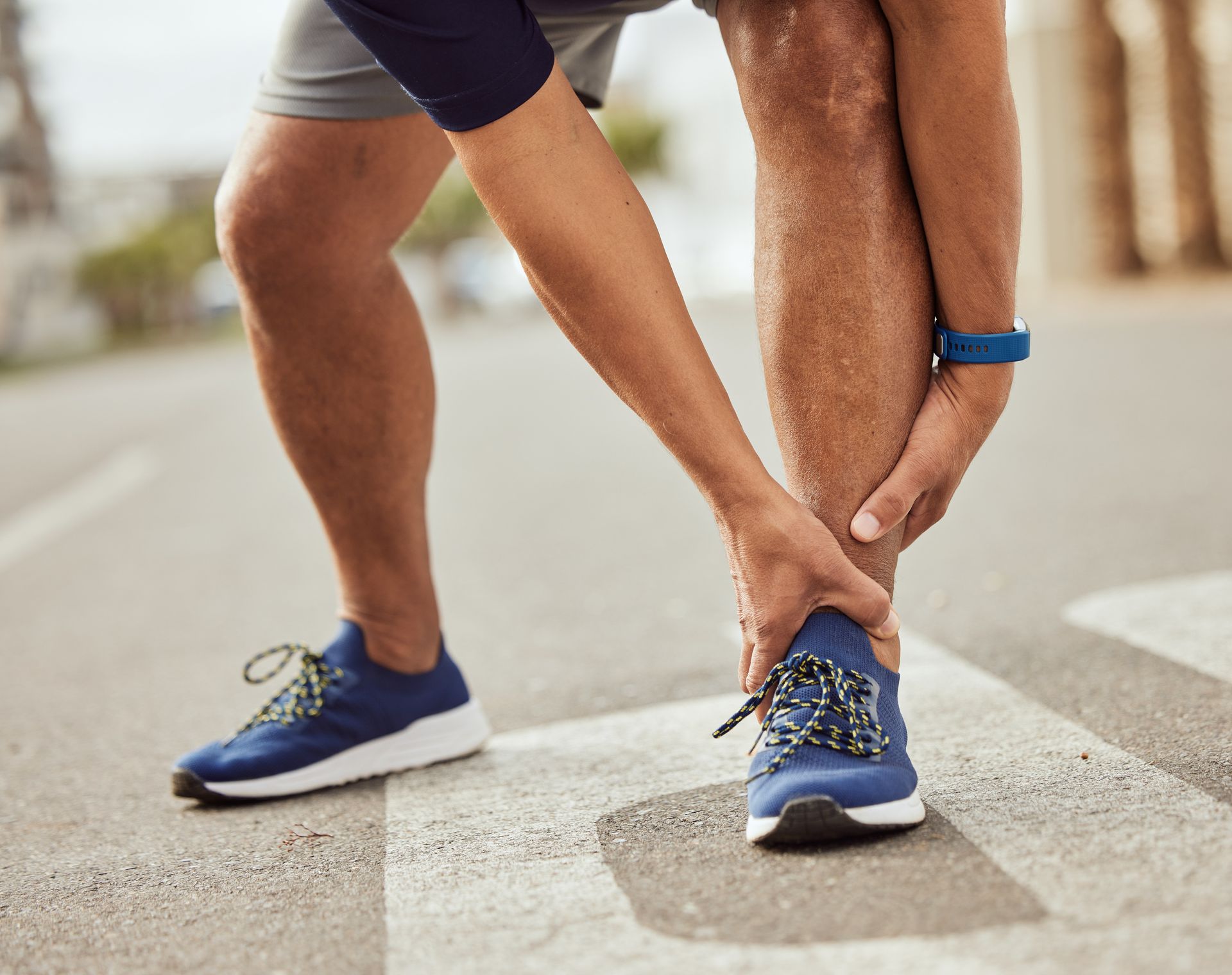 Runner tying shoelaces on blue sneakers at a crosswalk outdoors