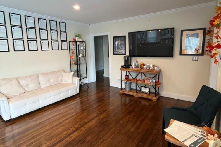 Living room with white sofa, wall-mounted TV, wooden floors, and a black chair by a small table