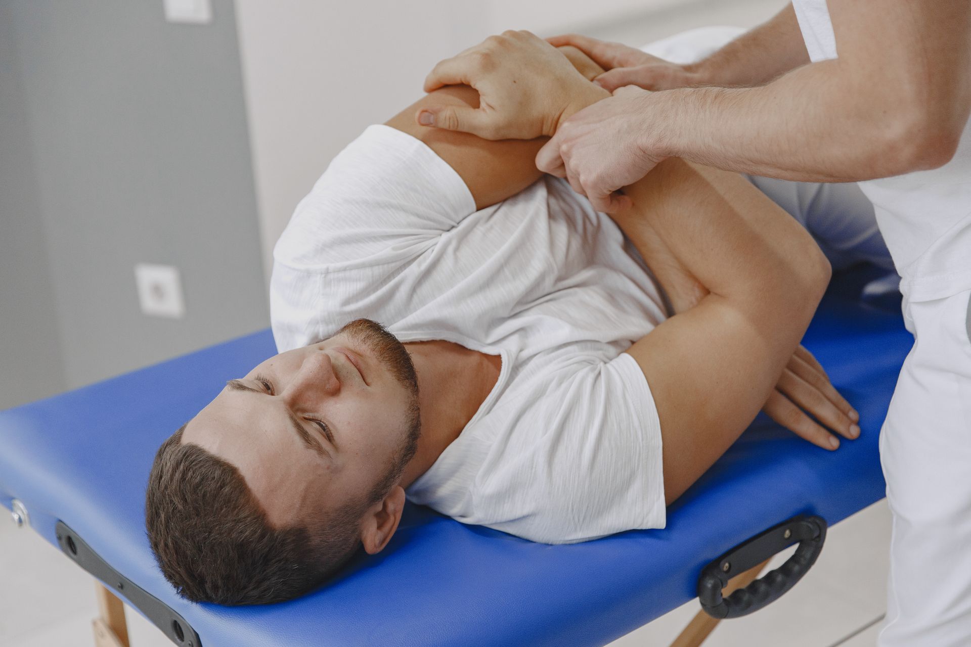 Man receiving a shoulder stretch on a blue treatment table in a clinical setting