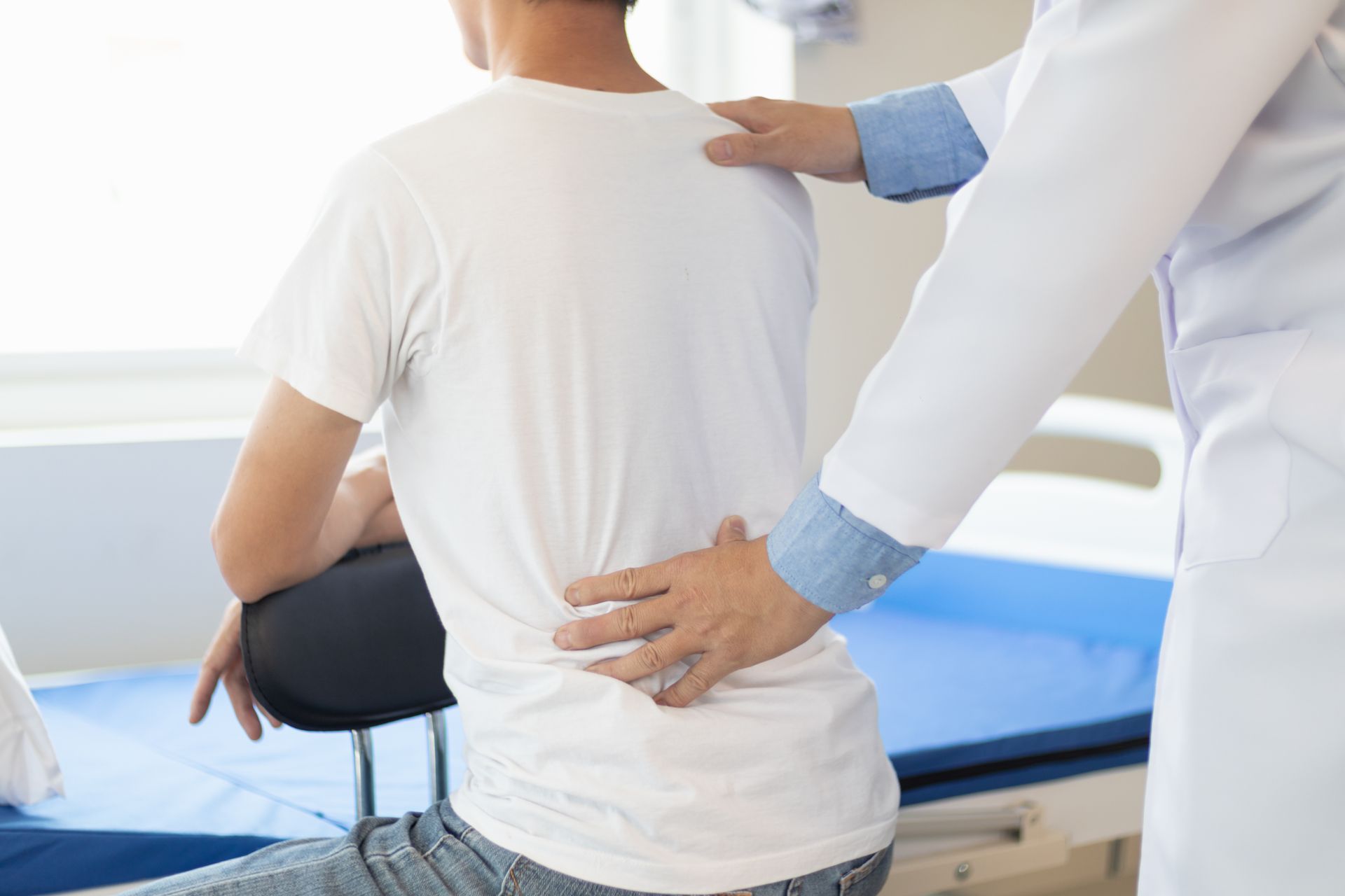 Doctor examining a seated patient’s back in a clinic exam room
