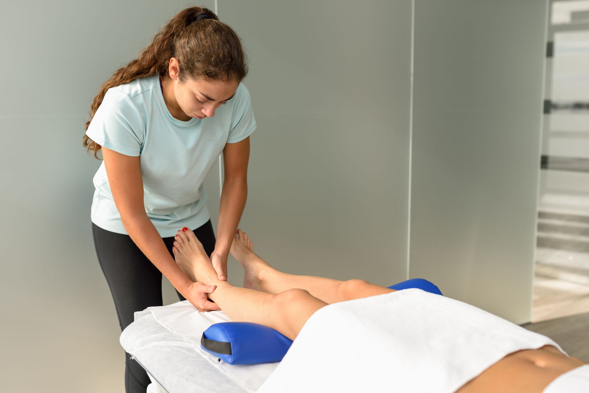 Massage therapist working on a client’s legs on a treatment table in a spa room