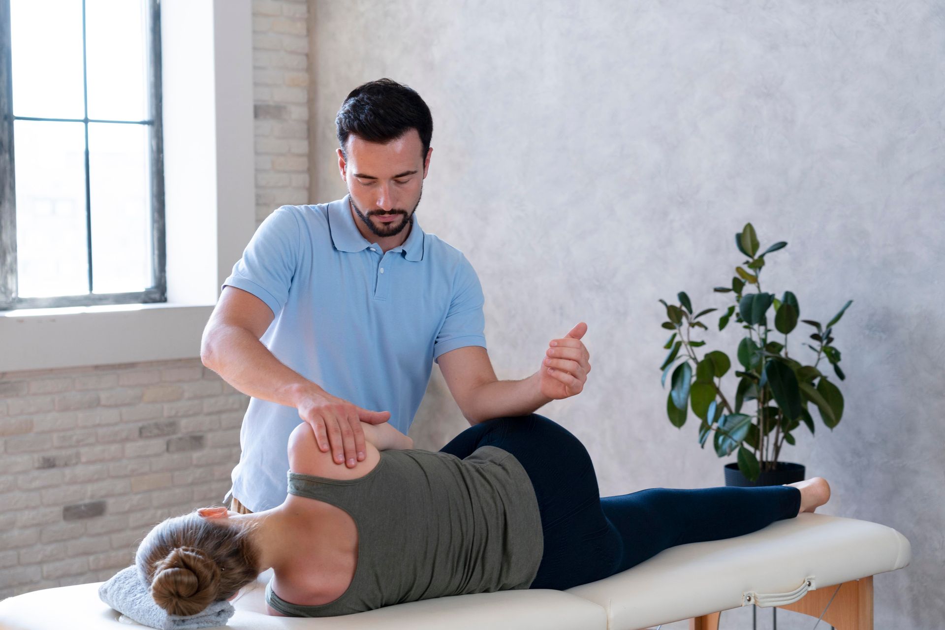 Therapist performing a back massage on a client on a treatment table in a bright room