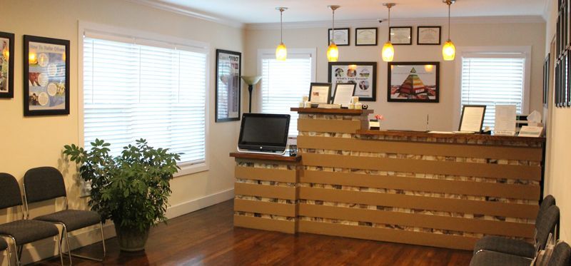 Waiting room with chairs, potted plant, framed art, and a wooden reception desk in a bright office