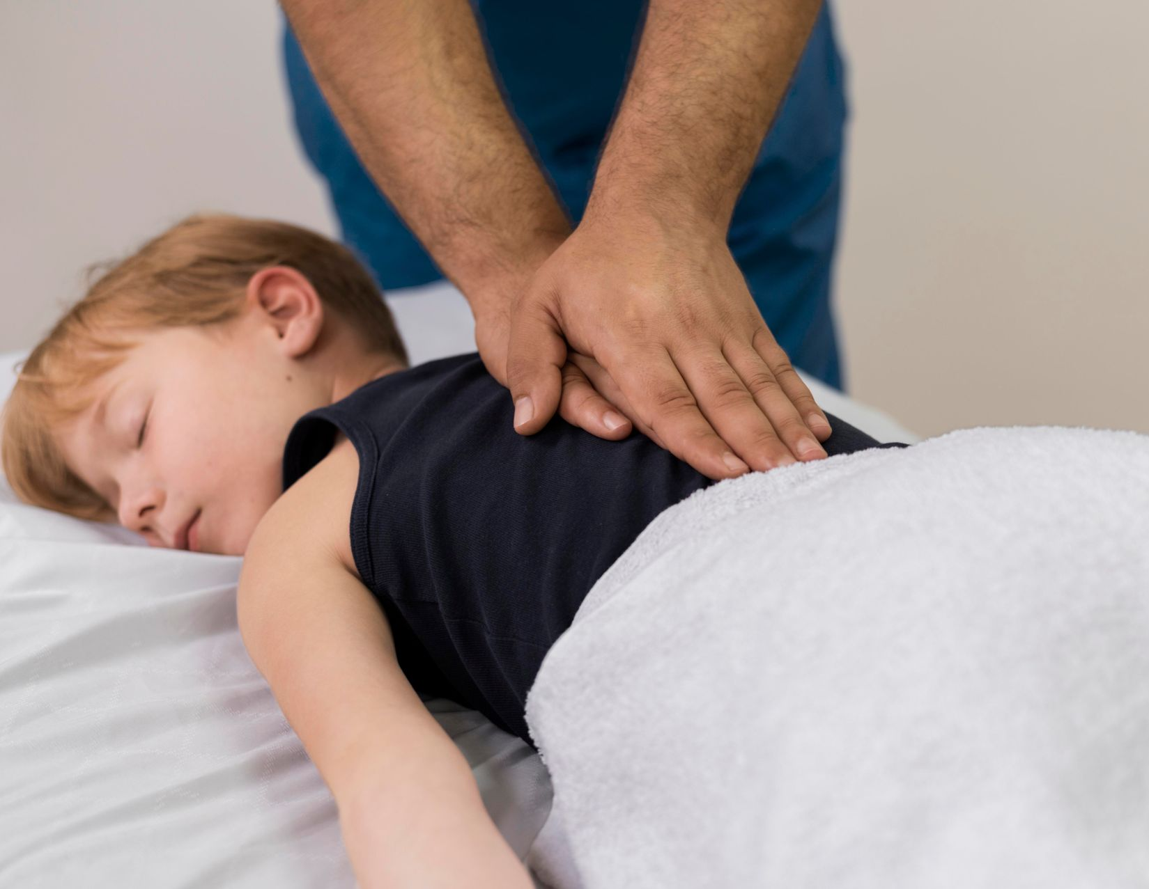 Hands pressing on a child’s back during a massage on a treatment table