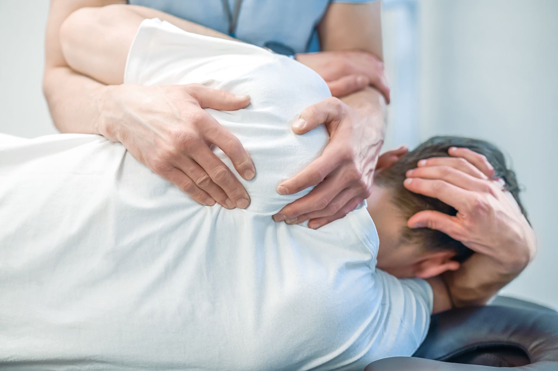 Person on a massage table receiving a back massage, holding their head in discomfort