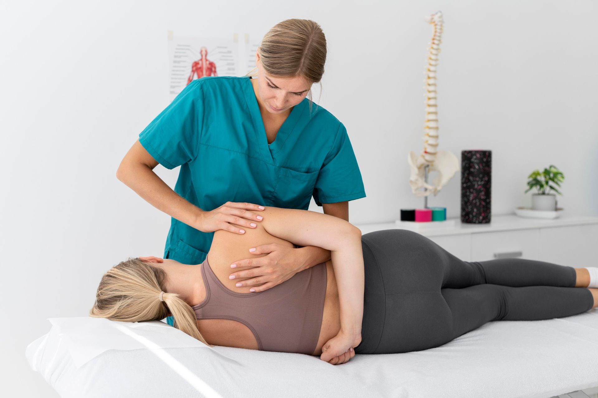 Therapist in teal scrubs performing a spinal adjustment on a patient lying on a table in a clinic