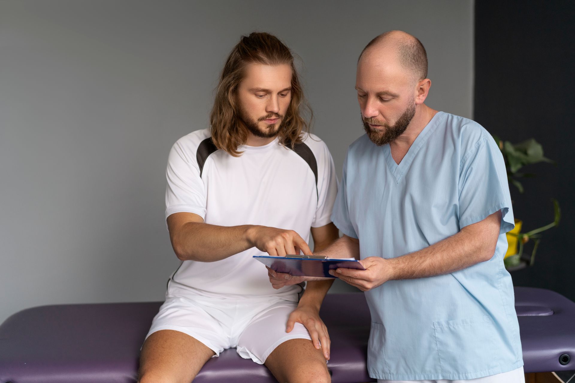 Two men in medical scrubs reviewing a tablet together on an exam table