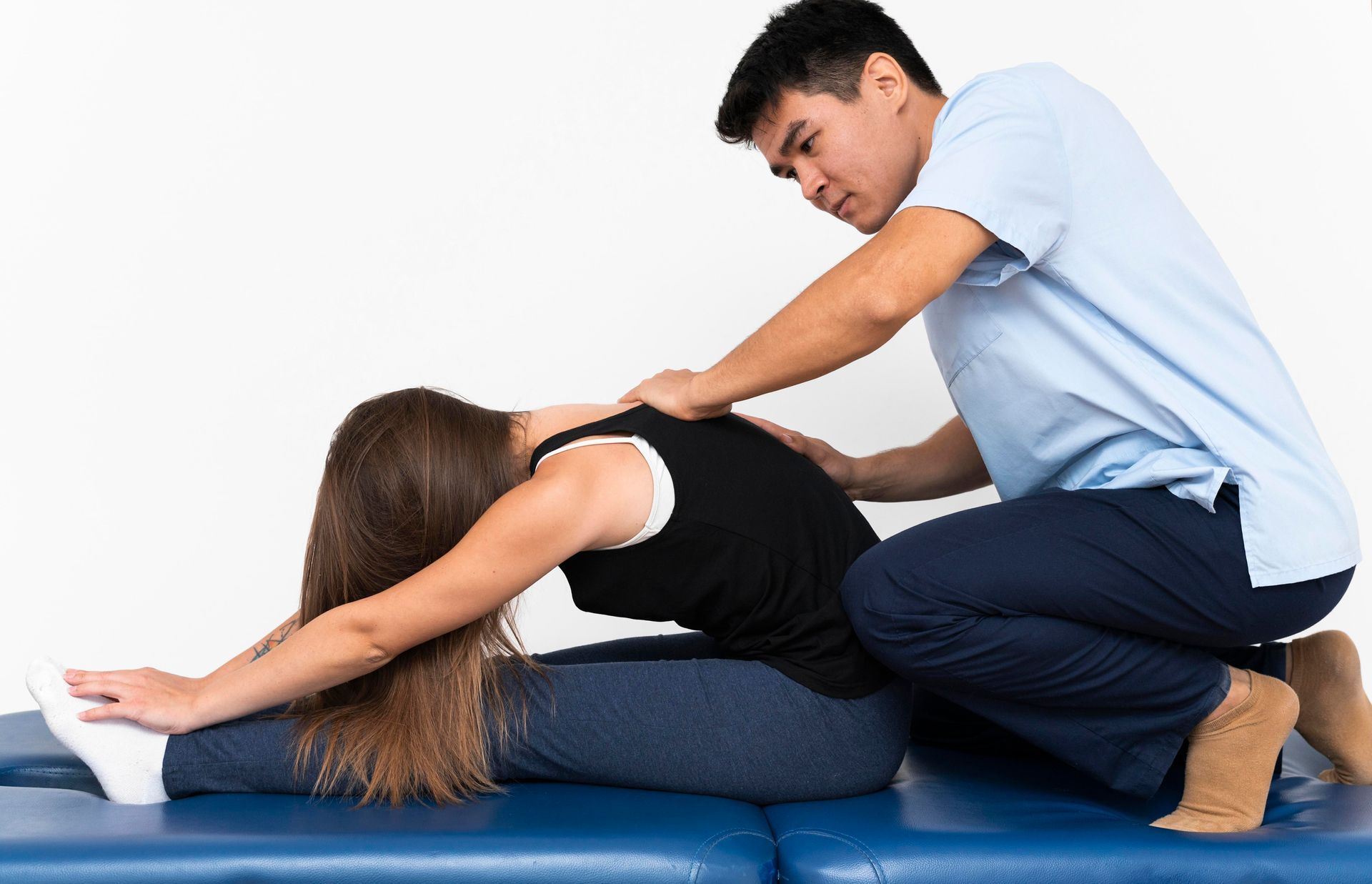 Physical therapist stretching a woman on a blue mat during a back stretch exercise