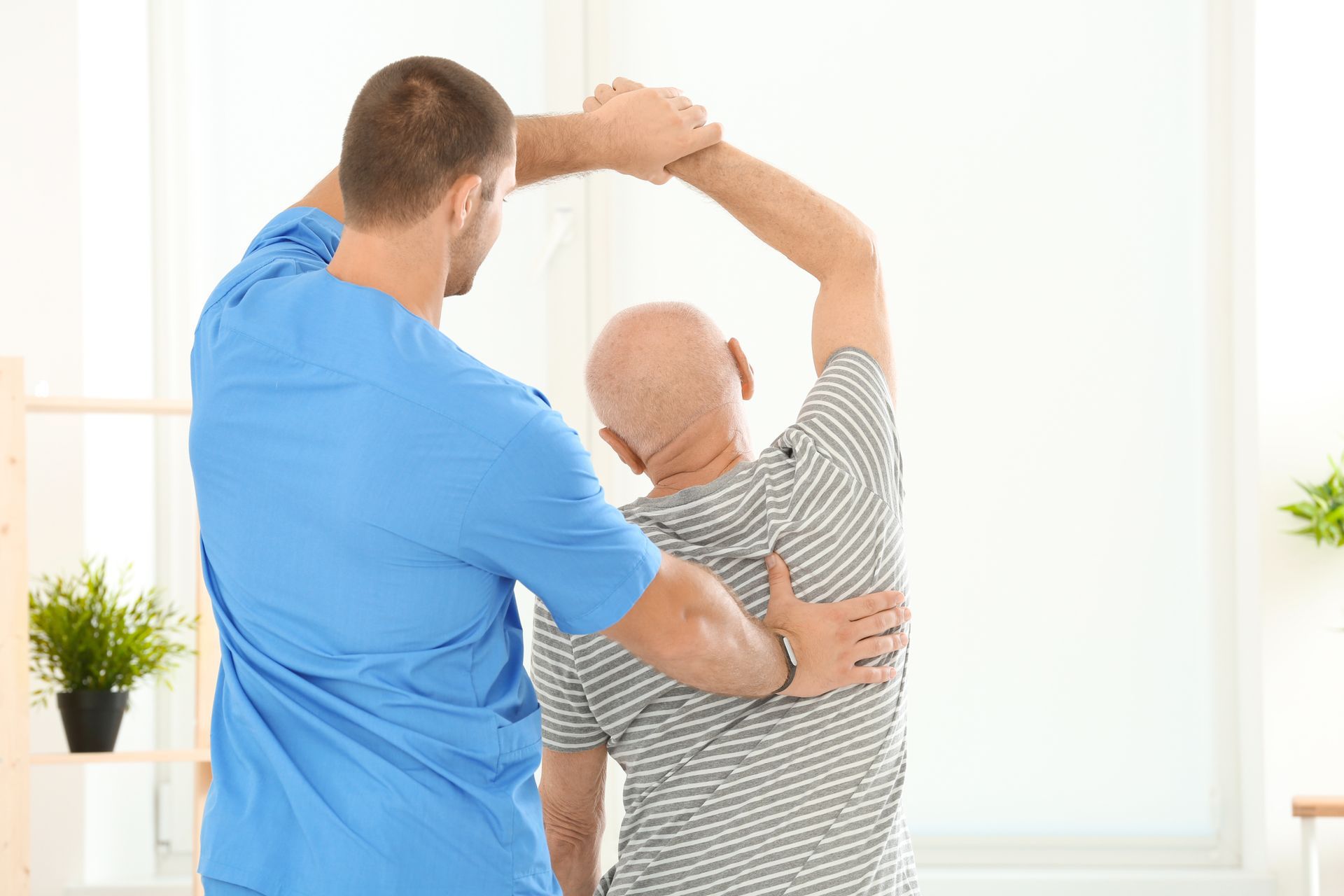 Man assisting a person with back stretch in a bright room