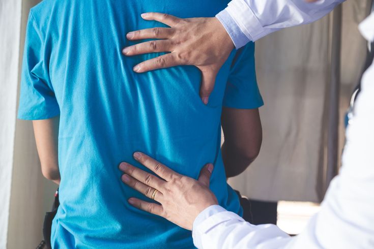 Physical therapist examining a patient’s back during treatment, with hands on upper and lower back.