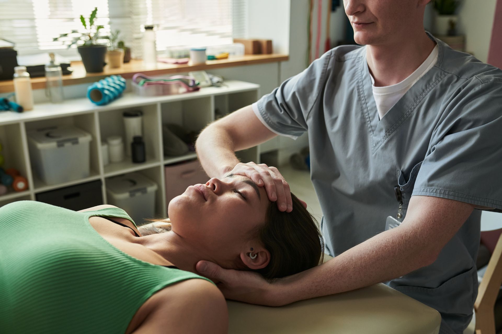 Therapist gently massages a client’s head and neck on a treatment table in a bright clinic room