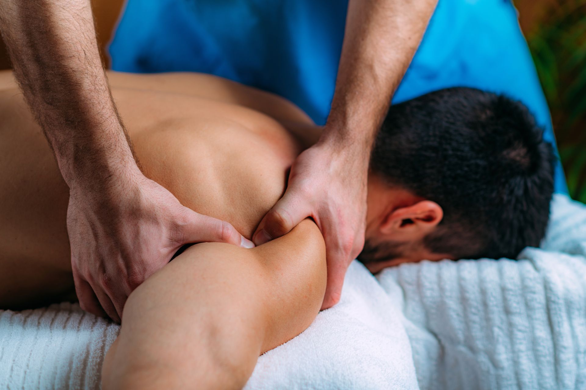 Massage therapist kneads a person’s neck and shoulders on a massage table