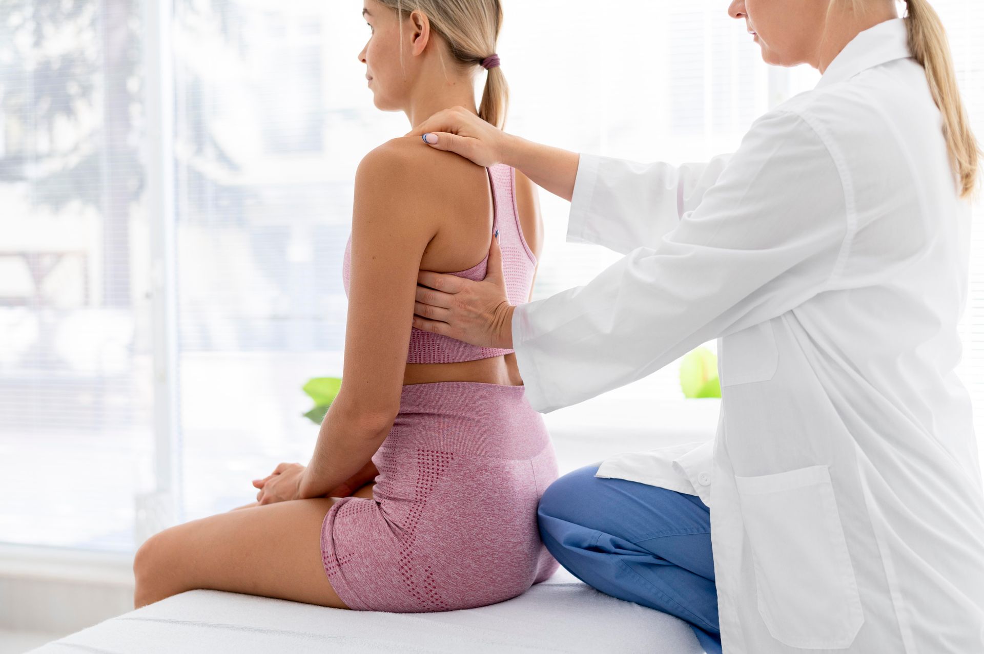 Physical therapist adjusting a seated patient’s back in a bright clinic room