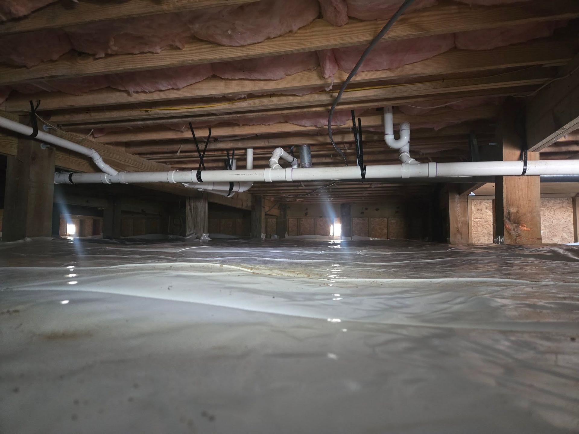 Flooded basement with standing water, exposed wooden beams, and white pipes overhead
