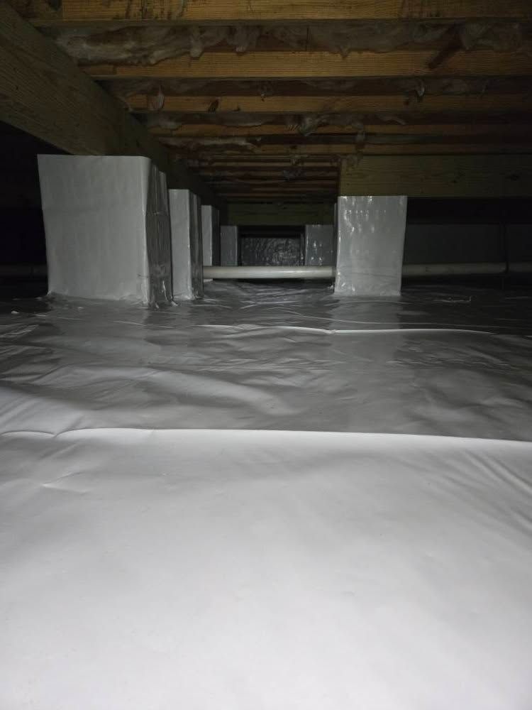 Low crawlspace with white plastic sheeting on the floor and wooden beams overhead