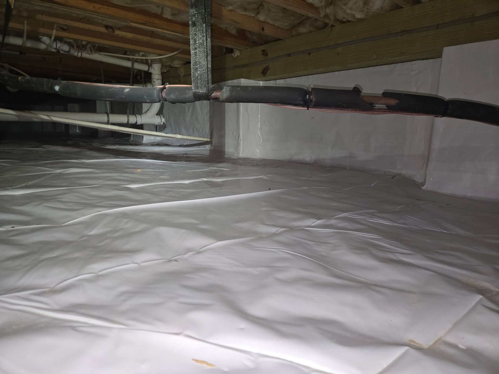 Plastic sheeting covering a basement floor beneath exposed beams and pipes