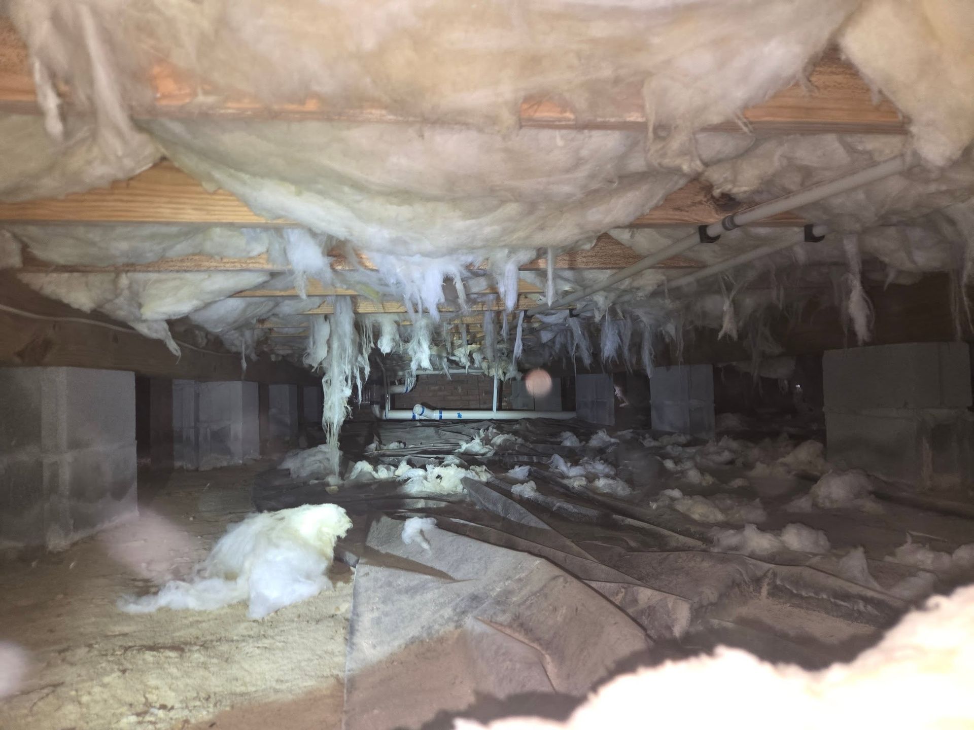 Icy crawlspace with insulation, hanging icicles, and debris on the ground