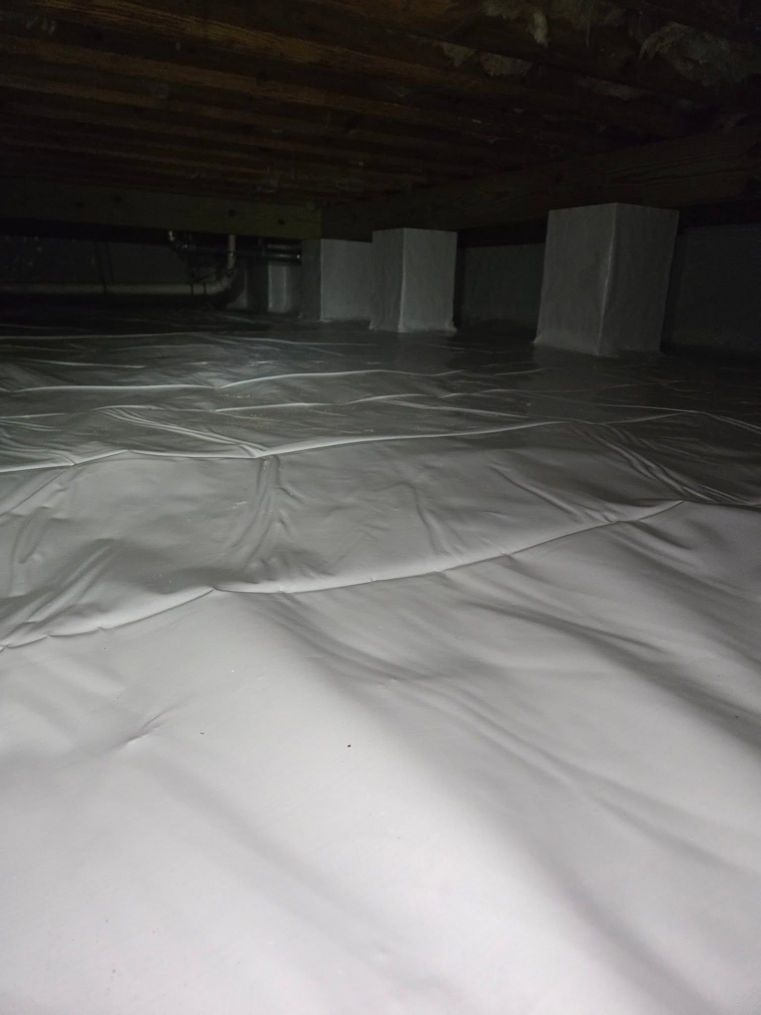 White plastic sheeting covers a dark attic floor with several white supports in the background.