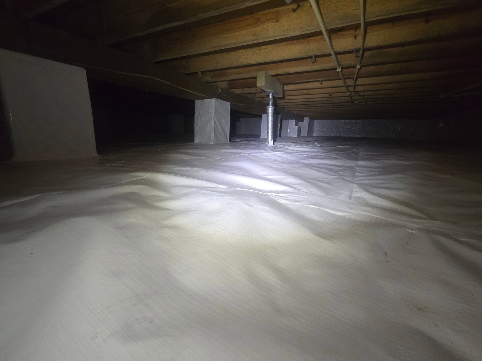 Dusty attic with exposed beams and pillars, lit by a flashlight beam across the floor