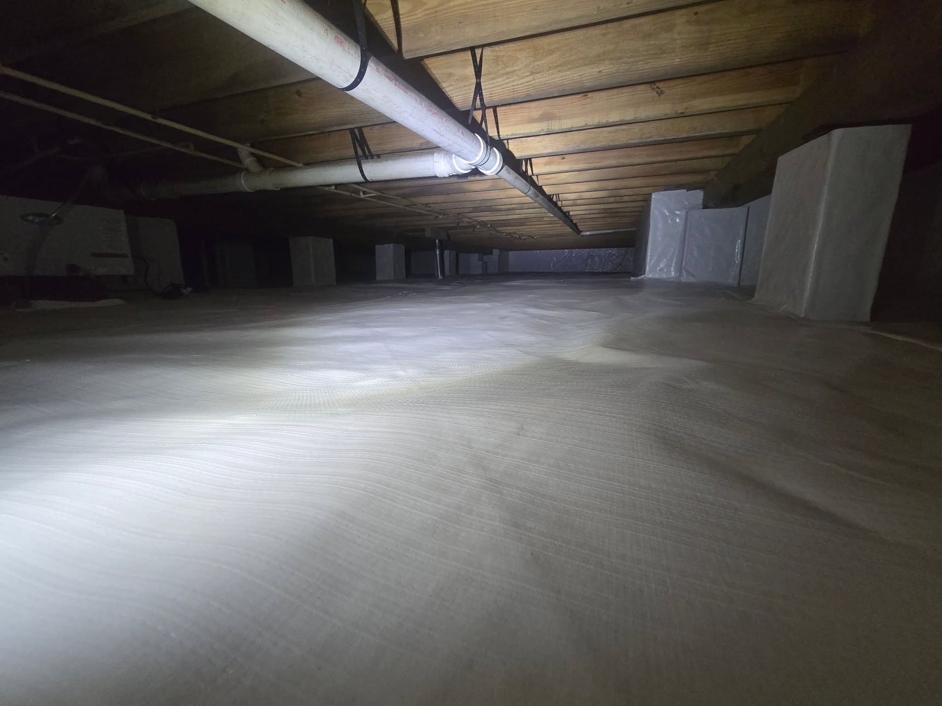 Dim empty industrial attic with exposed wooden beams and ductwork, lit by a flashlight or camera light.