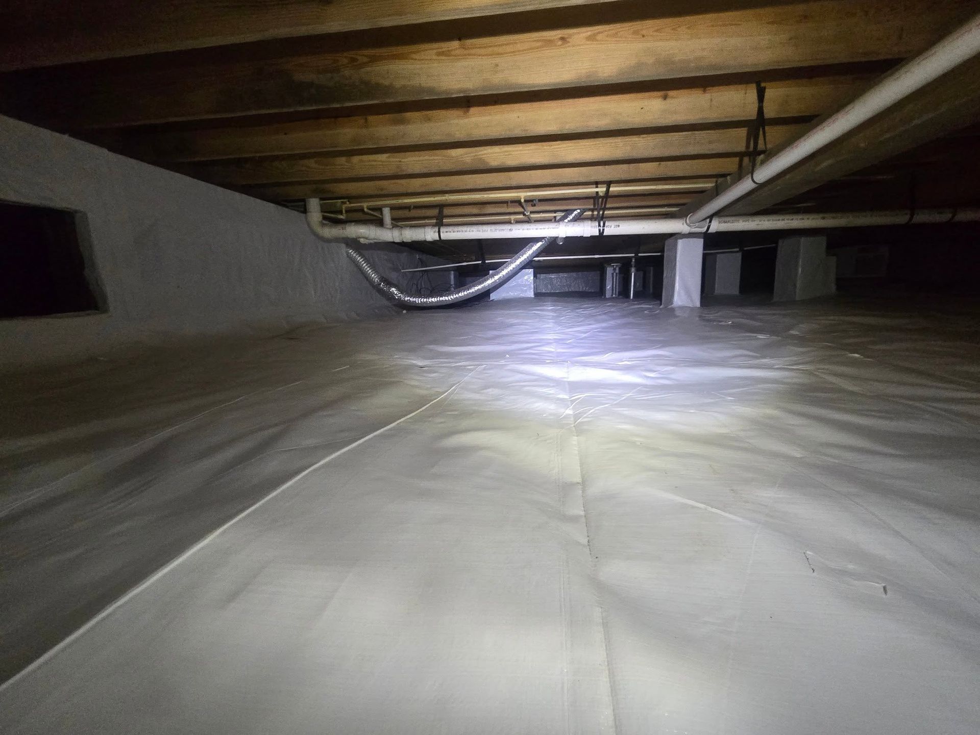 Dim attic crawlspace with exposed wooden beams and a bright flashlight beam on the floor
