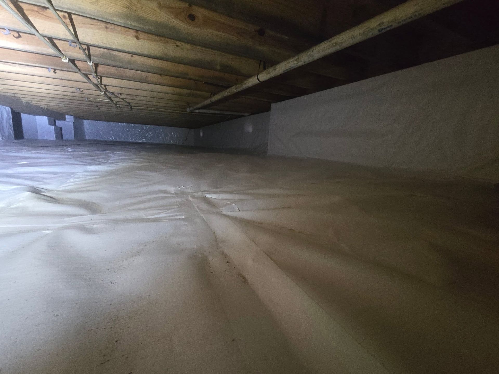 Crawlspace with plastic vapor barrier on the floor and exposed wooden joists overhead