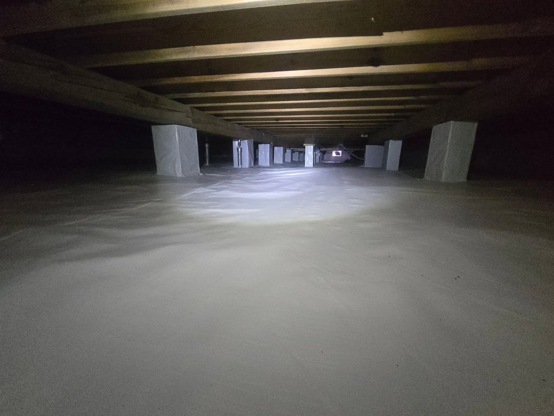 Low-ceiling concrete crawlspace with white pillars and a flashlight beam on the floor