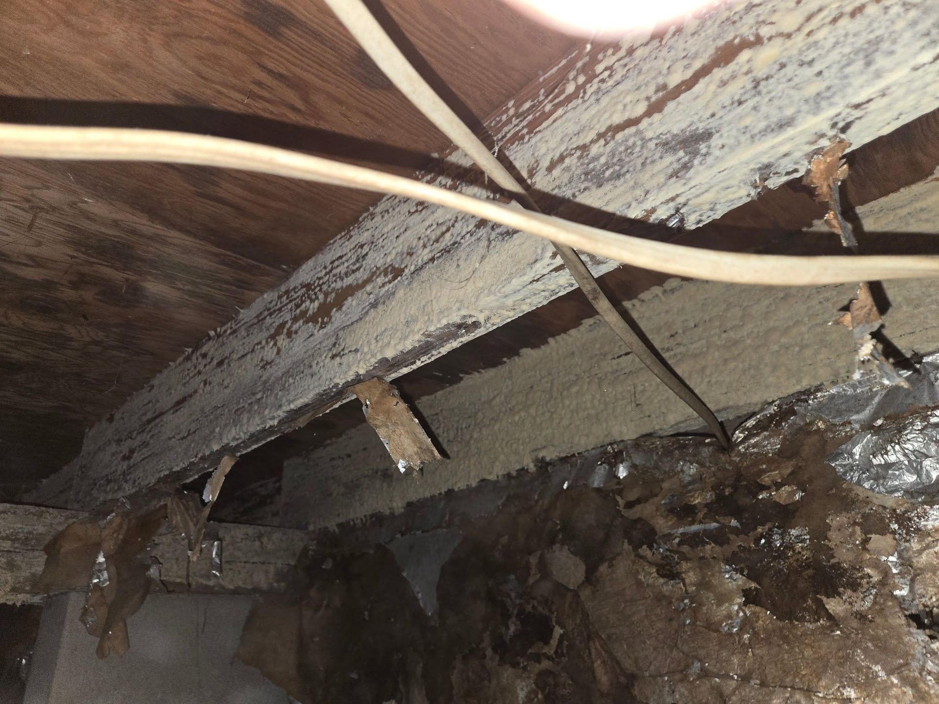 Damaged wooden ceiling with exposed beams, hanging wires, and water stains near a collapsed area