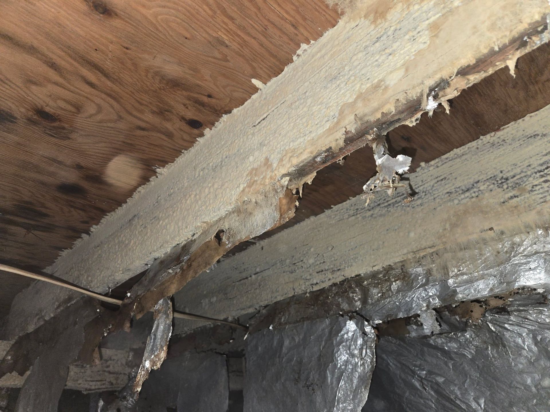 Damaged wooden ceiling with exposed insulation and broken plaster near a crack