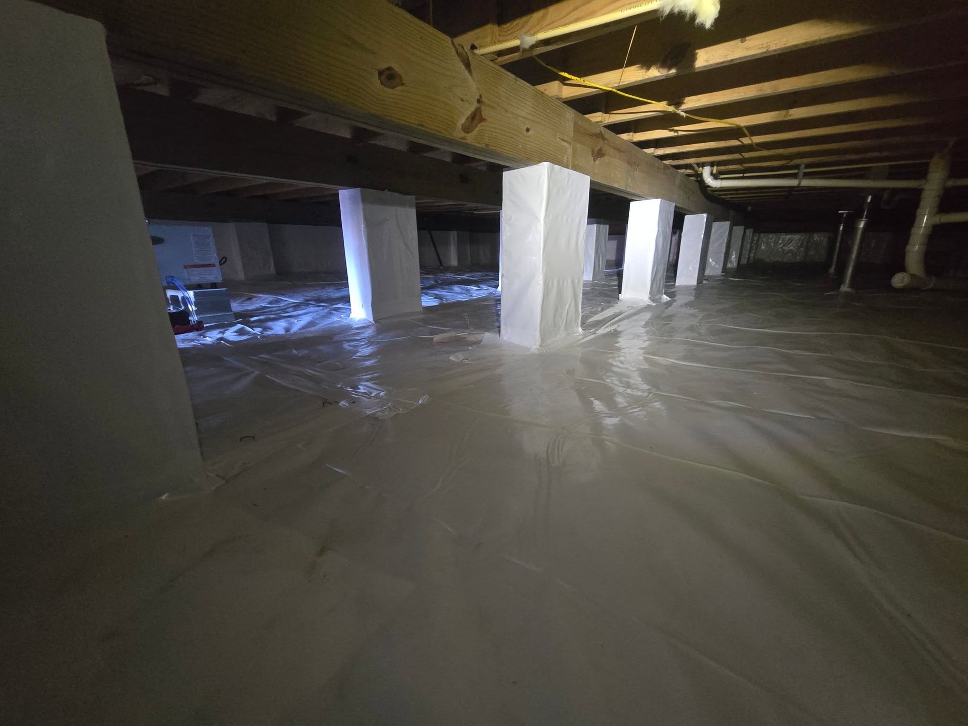 Flooded basement with shallow water, white support columns, and exposed ceiling beams