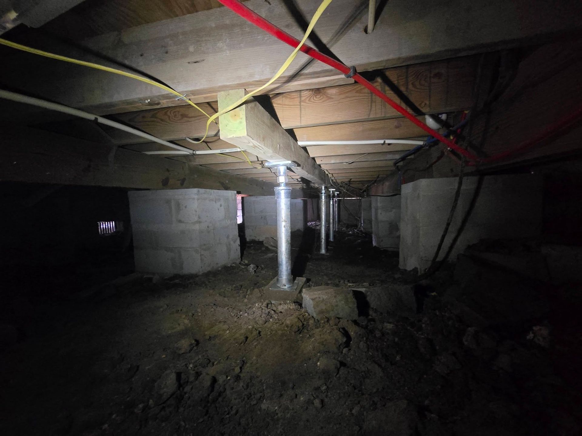 Dim crawlspace with exposed ducts, pipes, insulation, and dirt floor under a house.