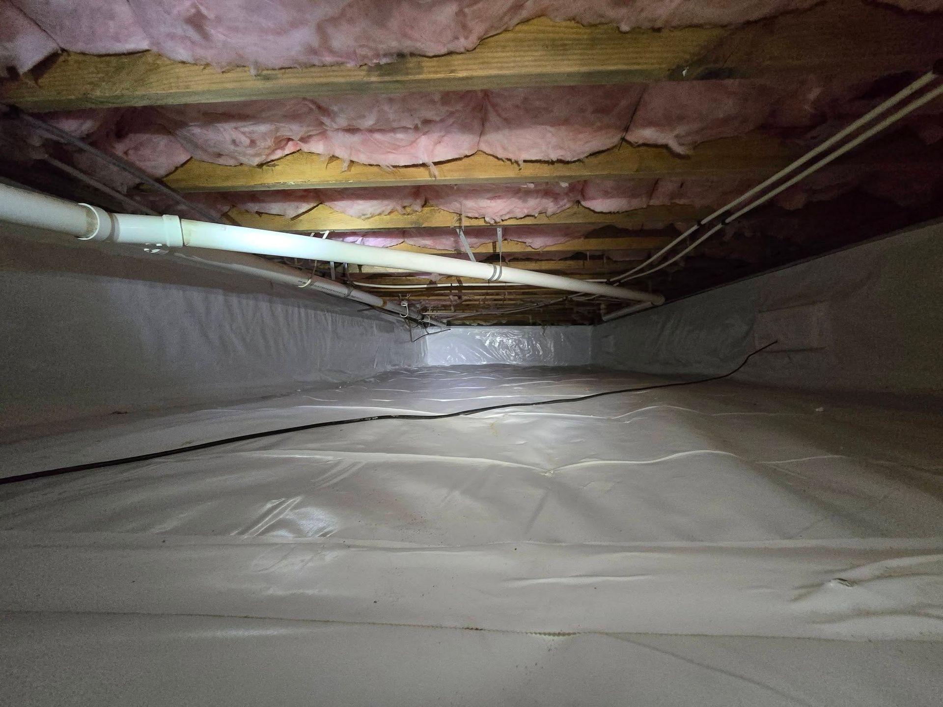 Insulated crawlspace with plastic vapor barrier on floor and pink fiberglass insulation overhead